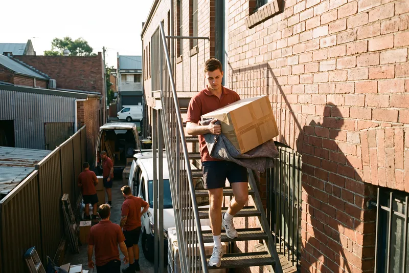 Mover carrying a box down the external stairs behind a shopfront